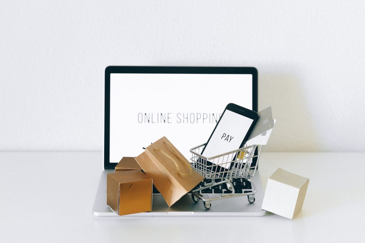 A miniature shopping cart and bags on a laptop, which reads “online shopping” on the screen.