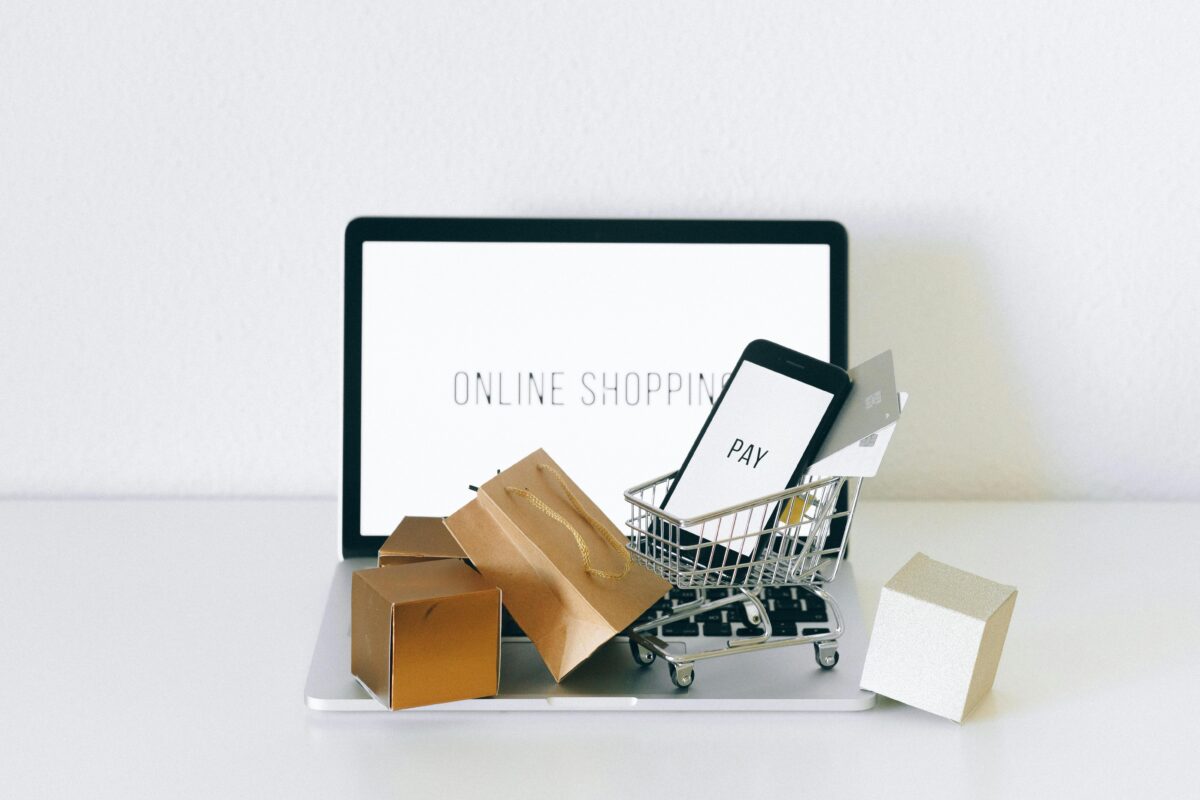 Un carro de compras y bolsas sobre una laptop con “online shopping” escrito en la pantalla.