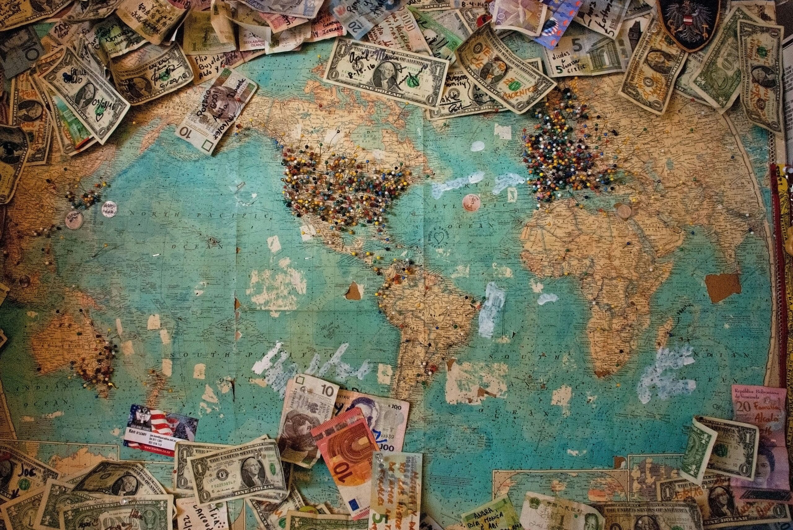 Old map with pins and currencies from all over the planet