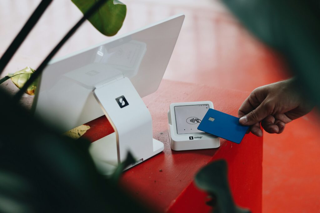 Una persona utiliza una tarjeta de crédito azul sobre una terminal de pago sin contacto en un punto de venta, lo que ilustra el procesamiento de tarjetas de crédito en acción.